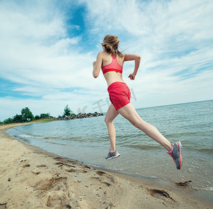 鞋子夏季摄影照片_年轻的女士在阳光灿烂的夏天砂沙滩上运行。锻炼。慢跑