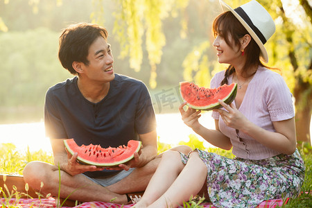 青年伴侣吃西瓜摄影照片_青年情侣坐在公园里吃西瓜