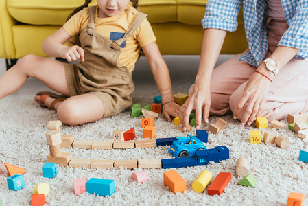 儿童和护士在地板上玩五颜六色的方块和玩具车的局部视图