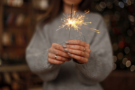 新年会议背景摄影照片_穿着针织毛衣的女人用女性手中惊人的火花来庆祝节日。特写. 
