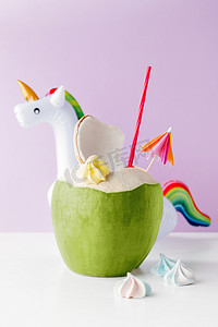 绿色时尚背景摄影照片_新鲜椰子在柔和的紫色背景与独角兽充气饮料持有人, 夏日的共鸣概念