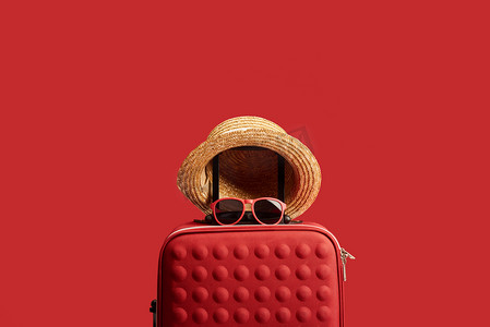 红色彩色旅行包与草帽和太阳镜隔离在红色 