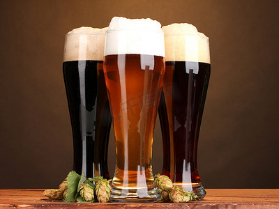 与不同的啤酒和棕色背景上的木桌上的跃点的三个眼镜
