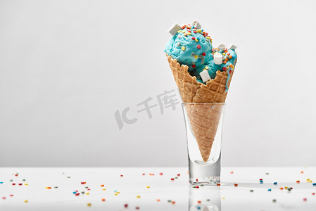 美味的甜蓝色冰淇淋与棉花糖和洒在脆华夫饼锥隔离在灰色