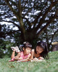 两个孩子躺在读一本书的草地上