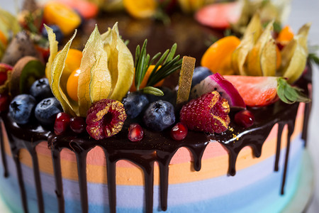 生日蛋糕背景横向摄影照片_同色的层数，饰以水果、 浆果和糖果的巧克力蛋糕。顶级 view.colorful 的美味蛋糕，五颜六色的奶油、 木制背景，把门关上，生日蛋糕甜点概念 