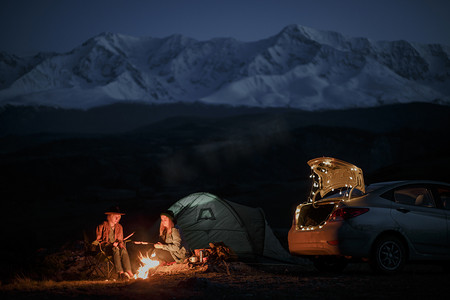 Couple in camping with campfire at night on mountain background