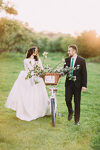 阳光明媚的衣服摄影照片_浪漫的新婚夫妇在阳光明媚的公园与装饰自行车摆姿势。温暖的太阳耀斑