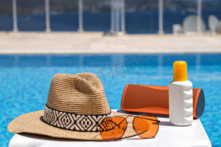 游泳池附近的橙色海滩饰物。防晒霜、太阳镜、音乐扬声器和草帽