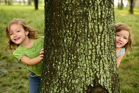 Two twin little girls playing in tree trunk