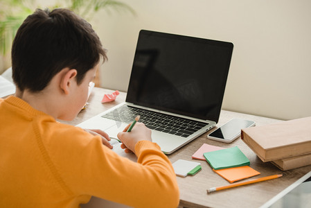 手机电脑屏幕摄影照片_小学生做家庭作业，而坐在办公桌附近的笔记本电脑与空白屏幕