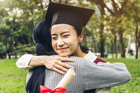 活动倒计时摄影照片_成功的学生年轻女子和学士礼服与文凭毕业生拥抱她的朋友在大学。庆祝毕业和教育理念