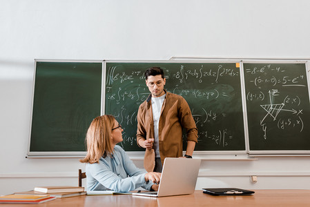 数学教师摄影照片_女教师在课堂上看学生和指着笔记本电脑 