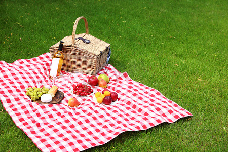 周末好摄影照片_园中的野餐篮，装有产品和酒瓶，铺在格子毯子上