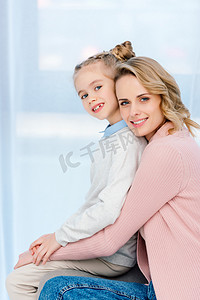 微笑的母亲和女儿拥抱和看照相机在家