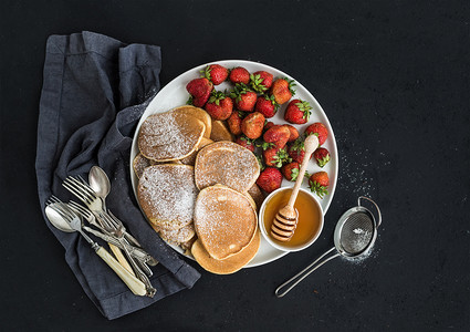 Breakfast plate. Homemade pancakes with fresh strawberry and honey, kitchen napkin, vintage silverware on dark grunge background. Top view