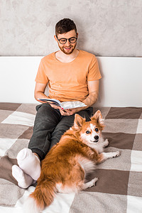 年轻人和他的狗在床上看书。垂直照片