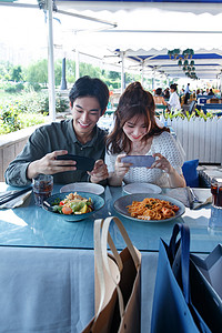 情侣吃饭摄影照片_青年情侣在餐厅里用手机拍照