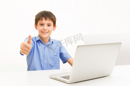 背景人物蓝色摄影照片_穿蓝色衬衣的男孩用一台笔记本坐在室内的桌子上