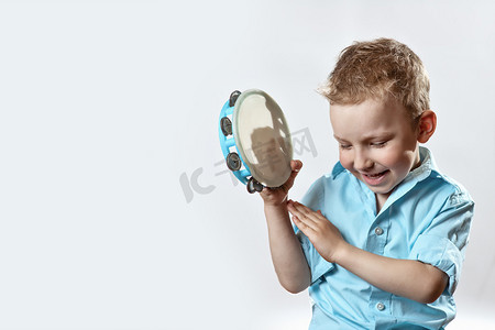 金牛会员摄影照片_一个穿着蓝色衬衫的开朗男孩，手里拿着一只金牛，在浅色背景上微笑着
