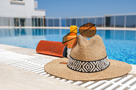 游泳池附近的橙色海滩饰物。防晒霜、太阳镜、音乐扬声器和草帽.