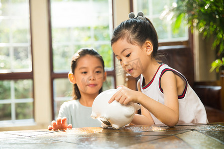 温馨桌子摄影照片_姐妹俩把钱放入存钱罐