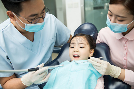 口腔器械摄影照片_男牙医和女牙医助手在为小女孩检查牙齿