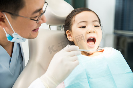 牙科诊疗室摄影照片_男牙医在为小女孩检查牙齿
