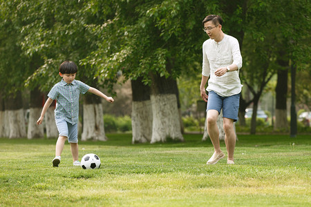 可爱奔跑摄影照片_快乐父子在草地上踢足球