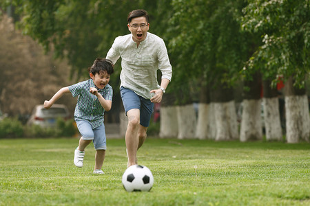 踢球父子摄影照片_快乐父子在草地上踢足球