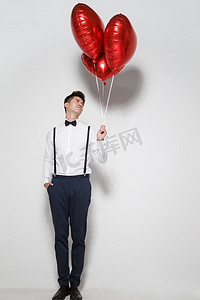 彩色爱心背景摄影照片_青年男人拿着心形气球