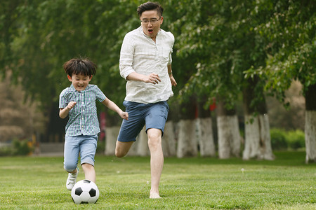 健康绿色环境摄影照片_快乐父子在草地上踢足球
