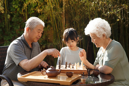 棋盘游戏摄影照片_老年夫妇和孙女在院子里下棋