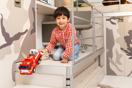 拿玩具汽车的男孩摄影照片_小男孩在卧室里拿着玩具车