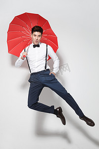 雨伞造型摄影照片_青年男人拿着心形红雨伞跳跃