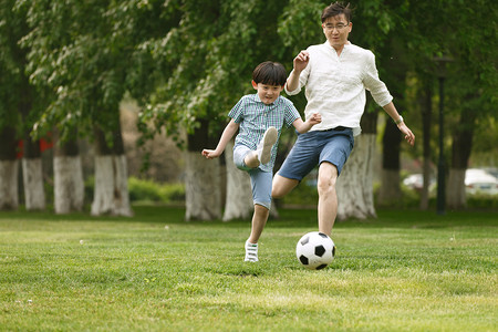 庭院草地摄影照片_快乐父子在草地上踢足球