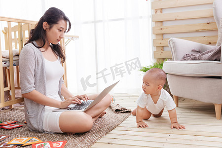 年轻妈妈在家边看孩子边使用电脑