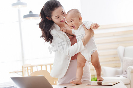 妈妈陪宝宝摄影照片_年轻妈妈抱着孩子在家办公