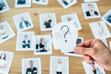 employment摄影照片_cropped view of man holding paper with human head and question mark near photos 