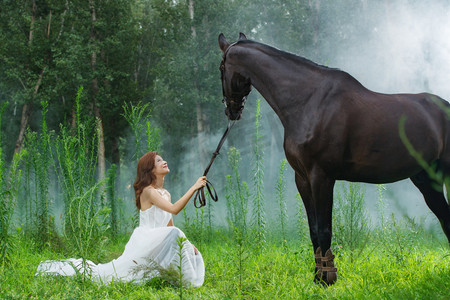 草地上穿婚纱的漂亮年轻女人和马