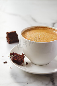 Crumbling chocolate brownie on latte coffee cup and saucer