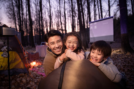 露营灯光摄影照片_幸福的父亲和两个孩子夜晚野外露营
