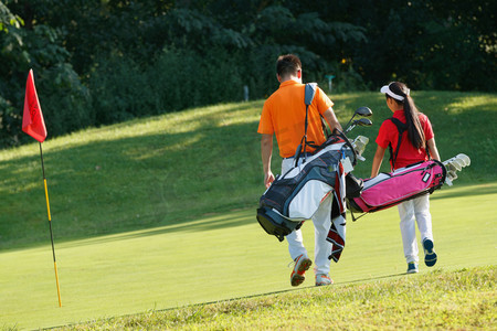 球场上教练和学生背着高尔夫球包步行的背影