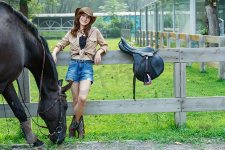 靠在围栏上的时尚个性女孩和吃草的马