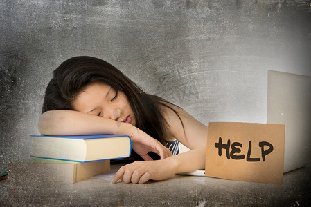 young pretty Asian Chinese woman student asleep on her laptop studying overworked with help sign on her desk