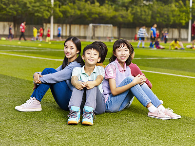 群快乐亚洲小学学生坐在草地上 