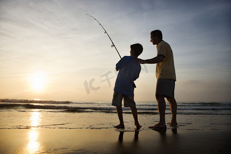 boy摄影照片_Man and young boy fishing in surf