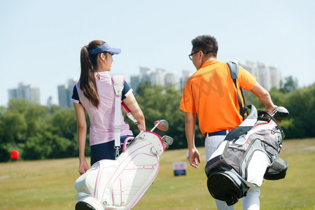 高尔夫球包摄影照片_青年人背着高尔夫球包在球场行走的背影