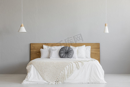 墙壁摄影照片_在木床上的针织毯子, 在最小的卧室内部与灯的灰色墙壁。真正的照片与一个地方为您的床头柜