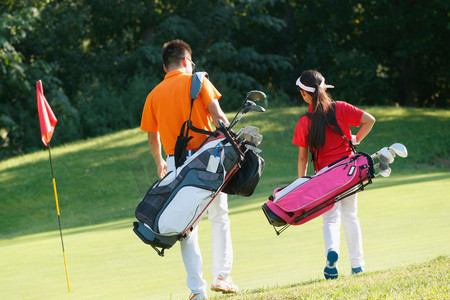 球场上教练和学生背着高尔夫球包步行的背影